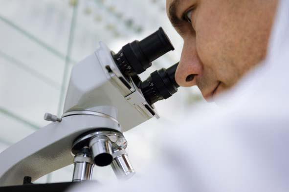 Nahaufnahme eines Forschers, der durch das Okular eines Mikroskops schaut, mit einem unscharfen Laborhintergrund.