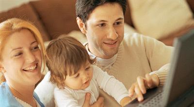 Eine Familie mit einem Kleinkind schaut gemeinsam auf einen Laptop. Die Eltern lächeln, während das Kind neugierig agiert.